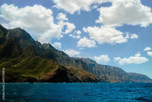 View of Na Pali coast of the island of Kauai in Hawaii from the sea with mountains and ocean as background and marshmallow clouds. © Emanuele