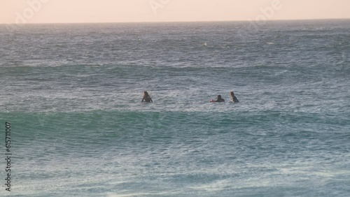 Three surfers waiting in calm ocean at sunset looking for waves photo