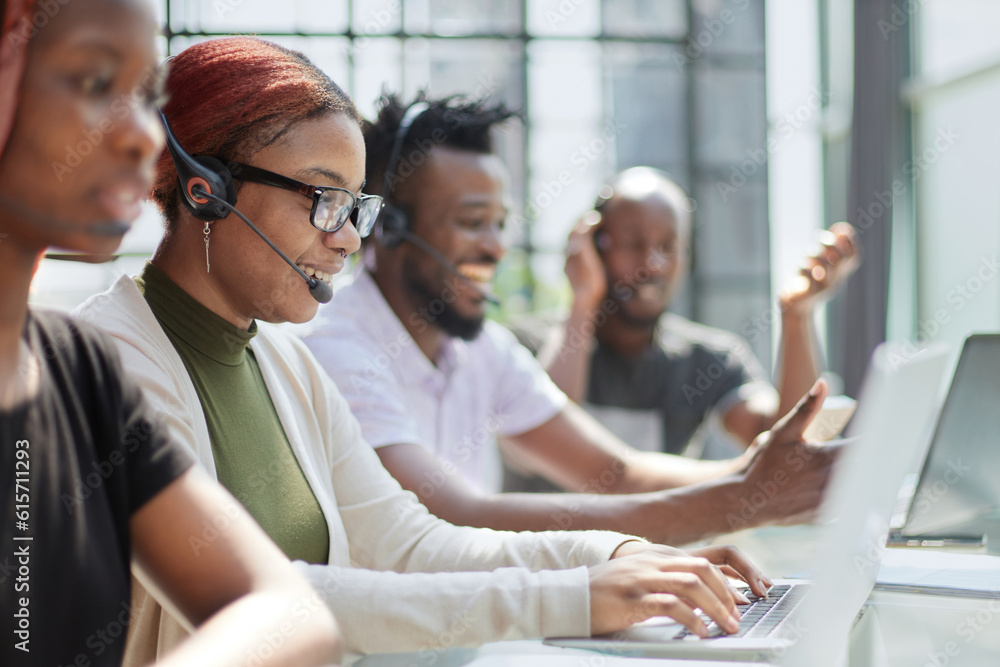 Fototapeta premium Smiling beautiful African American woman working in call center with diverse team