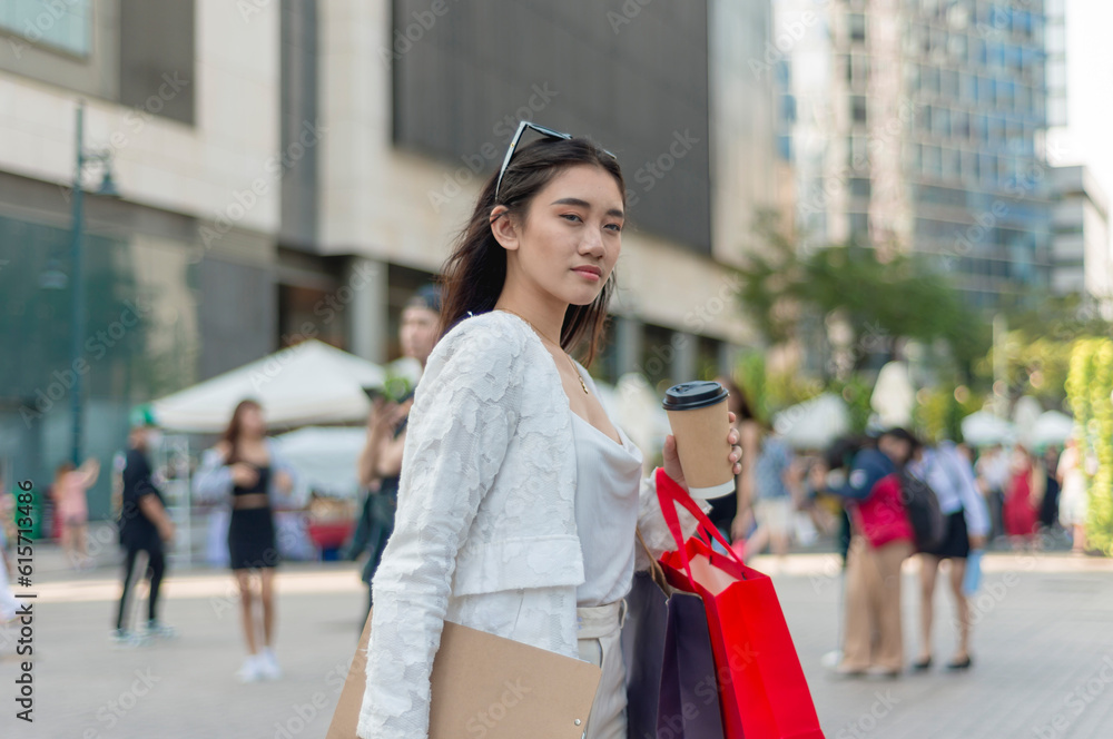 A pretty asian female office employee taking a walk to work at the city business district. Holding a cup of coffee and some shopping bags.
