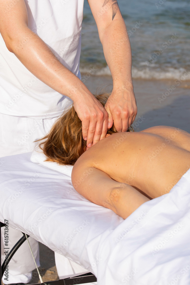 Woman having relax in tropical massage spa on the beach near the sea on massage table. Professional masseur provides back and neck spa procedures.