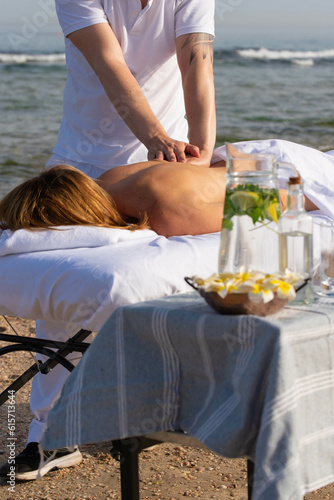 Woman having relax in tropical massage spa on the beach near the sea on massage table. Professional masseur provides back and neck spa procedures.