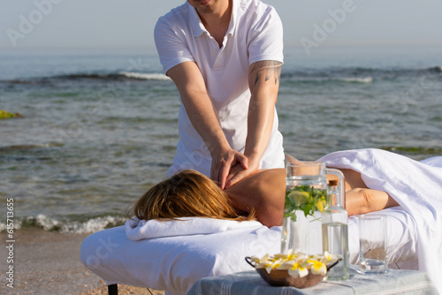 Woman having relax in tropical massage spa on the beach near the sea on massage table. Professional masseur provides back and neck spa procedures.