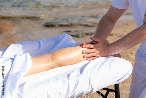 Woman having relax in tropical massage spa on the beach near the sea on massage table. Professional masseur provides leg and foot spa procedures.