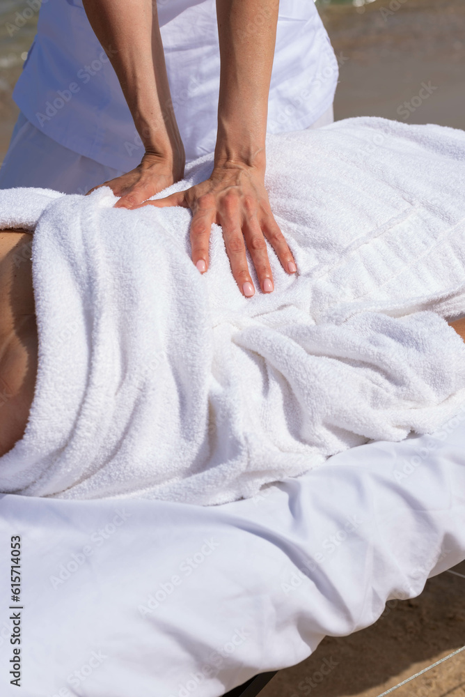 Woman having relax in tropical massage spa on the beach near the sea on massage table. Professional masseur provides neck, face and chest spa procedures. Woman having relax in tropical massage spa on the beach near the sea on massage table. Professional masseur provides neck, face and chest spa procedures.
