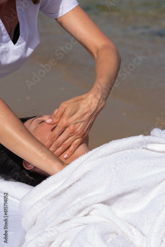 Woman having relax in tropical massage spa on the beach near the sea on massage table. Professional masseur provides neck, face and chest spa procedures.