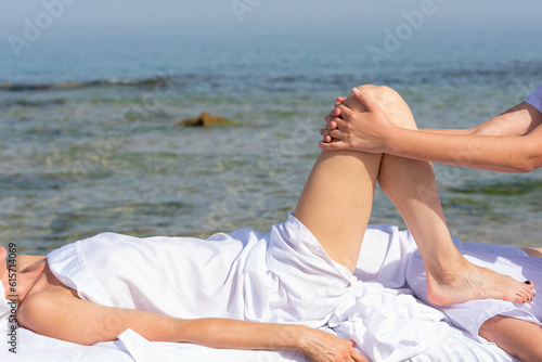 Woman having relax in tropical massage spa on the beach near the sea on massage table. Professional masseur provides leg and foot spa procedures.