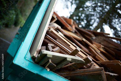 green recycling container filled with wood, next to a house