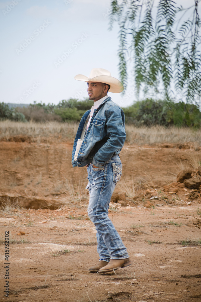 Cowboy wearing jeans and a hat, standing under the sky with fluffy clouds, working on a farm Cowboy wearing jeans and a hat, standing under the sky with fluffy clouds, working on a farm
