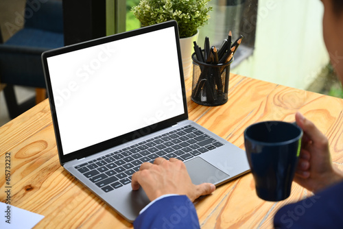 Closeup shot businessman drinking hot coffee and using laptop on wooden office desk