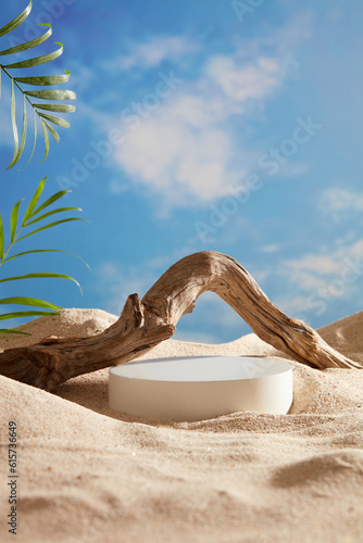 A white podium in round-shaped displayed on the sand with a big tree branch and some green tropical leaves. Blue sky background