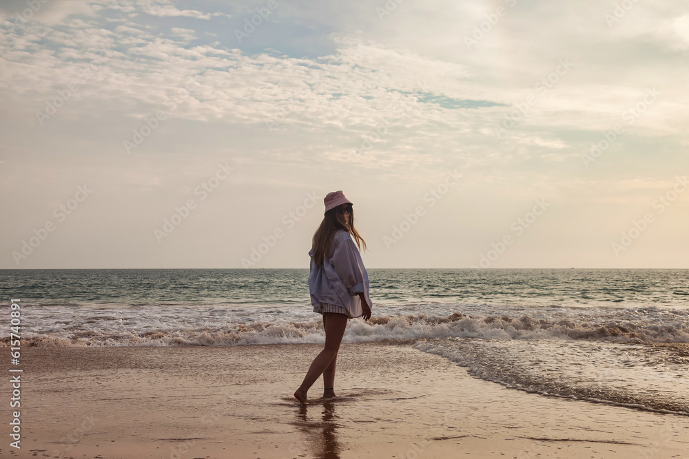Full length of young woman walking on tropical sea beach at waves background. Cute lady in beachwear relaxing and enjoying, posing in tropics coast. Travel vacation holiday concept. Copy ad text space