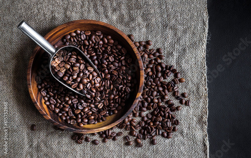 Coffee beans composition with metal scoop and burlap bag on dark background, top view. Stillife with heap of roasted Arabica grains in wooden bowl, decor for coffee shop.