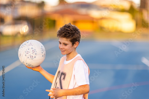 young boy wearing netball bib and holding ball on blue court photo