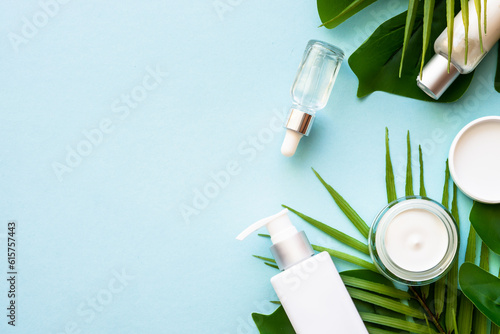 Natural cosmetic products. Cream, serum, tonic with green tropical leaves. Flat lay on blue background with space for design.