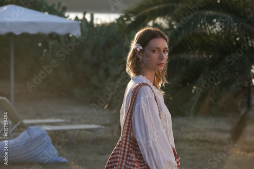 Portrait of young woman in linen blouse holding beach bag in the resort during summer vacation