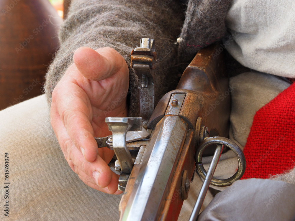 The bolt of a flintlock rifle in the hands of the shooter, hands and a gun close-up. Historical reconstruction of a military camp.