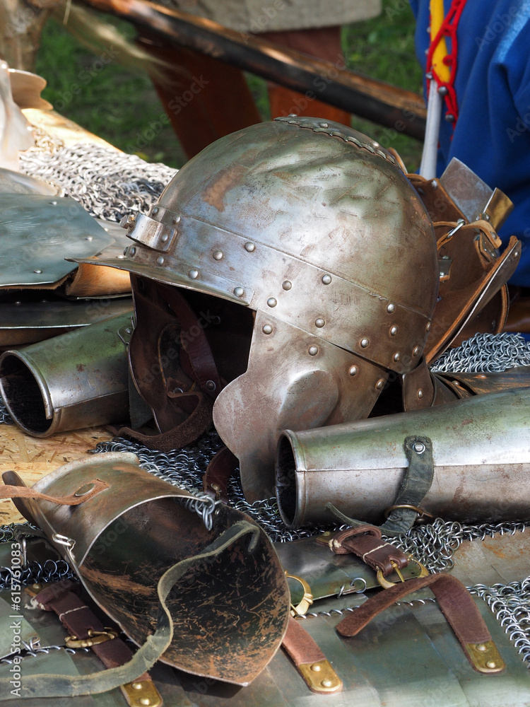 Knight's helmet and ammunition items of a medieval warrior on a rough wooden table, close-up. Historical reconstruction of a military camp.