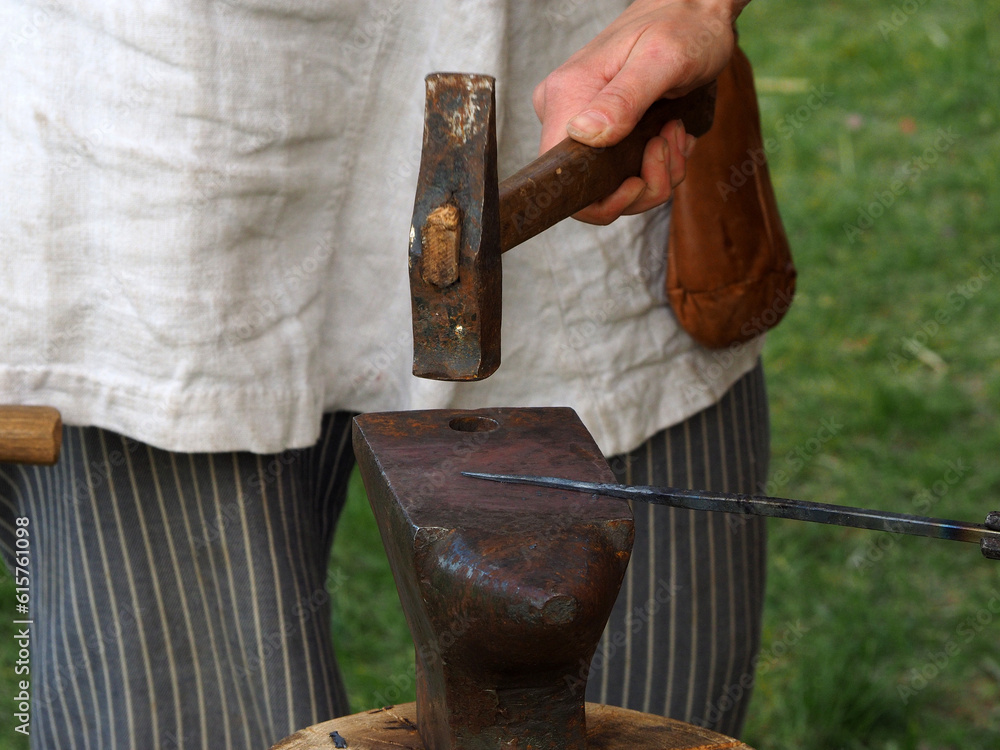 A blacksmith armorer makes a spear tip with a hammer and an anvil. Historical reconstruction of a military camp.