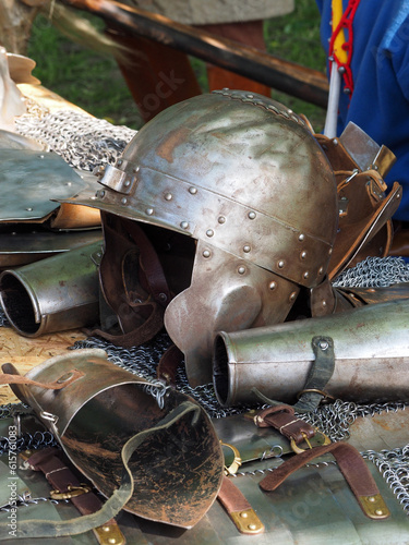 Obraz na płótnie Knight's helmet and ammunition items of a medieval warrior on a rough wooden table, close-up. Historical reconstruction of a military camp. w salonie