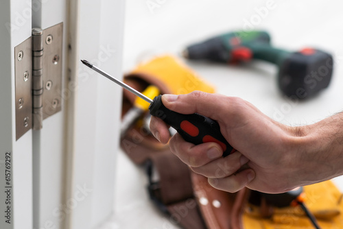 A locksmith is repairing an interior door lock. Close-up of male hands repairing or replacing an entrance door lock with a hex screwdriver photo