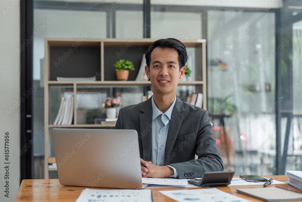 Happy smiling business man company executive ceo manager wearing suit sitting at desk in office working on laptop computer at workplace