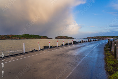 A dark storm cloud advancing over a causeway road next to a coastal bay