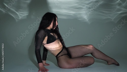A brunette girl in black underwear with a beautiful athletic figure poses in a dark studio with light, lies on the floor in pantyhose