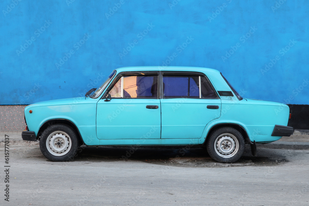 A Monochrome photo of a blue car in front of a blue wall in Havana Cuba