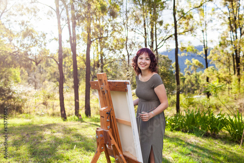 Smiling portrait of young australian artist standing beside canvas on easel photo