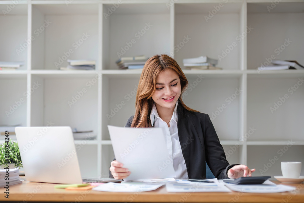 A beautiful young Asian businesswoman in a formal business suit is using her laptop and working on marketing reports at her desk in the office.