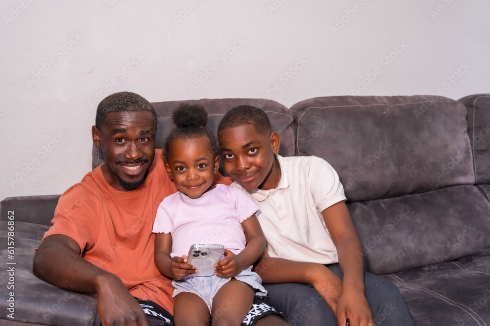African black ethnic family father with children on sofa at home looking at phone