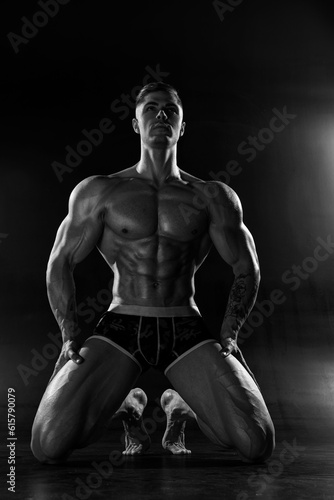 Muscular shirtless man with perfect body posing kneeling in studio