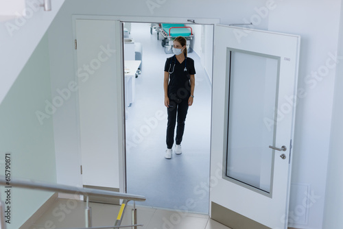 A female doctor walks down the corridor of the clinic. A young woman in a surgeon s suit and a medical mask.