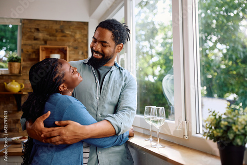 Happy black man and his wife embracing while talking by window.