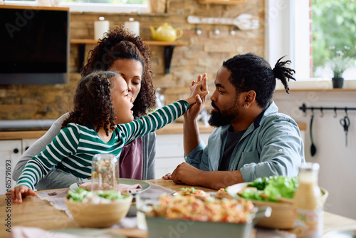 Little black girl and her parents communicating at dining table.