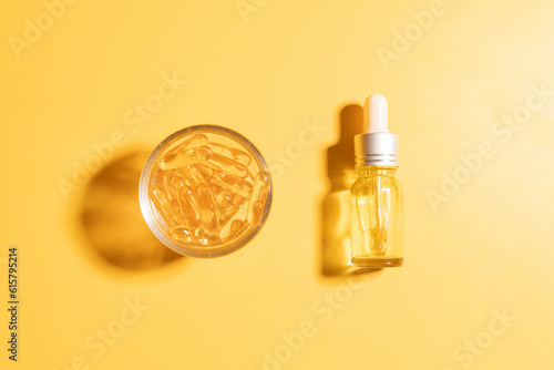 Oil capsules and serum bottle with dropper on yellow background. Nutritional supplement contains fish oil, omega 3, omega 6, omega 9, vitamin e, vitamin d and vitamin. Health care and beauty concept.