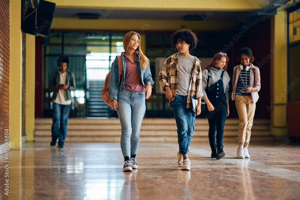 Happy high school friends talk while walking through hallway at school.