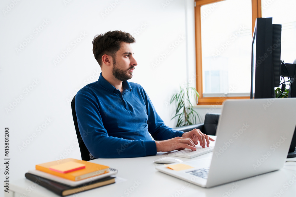 Male programmer working at a desk with laptop and external monitor freelancing from home Male programmer working at a desk with laptop and external monitor freelancing from home