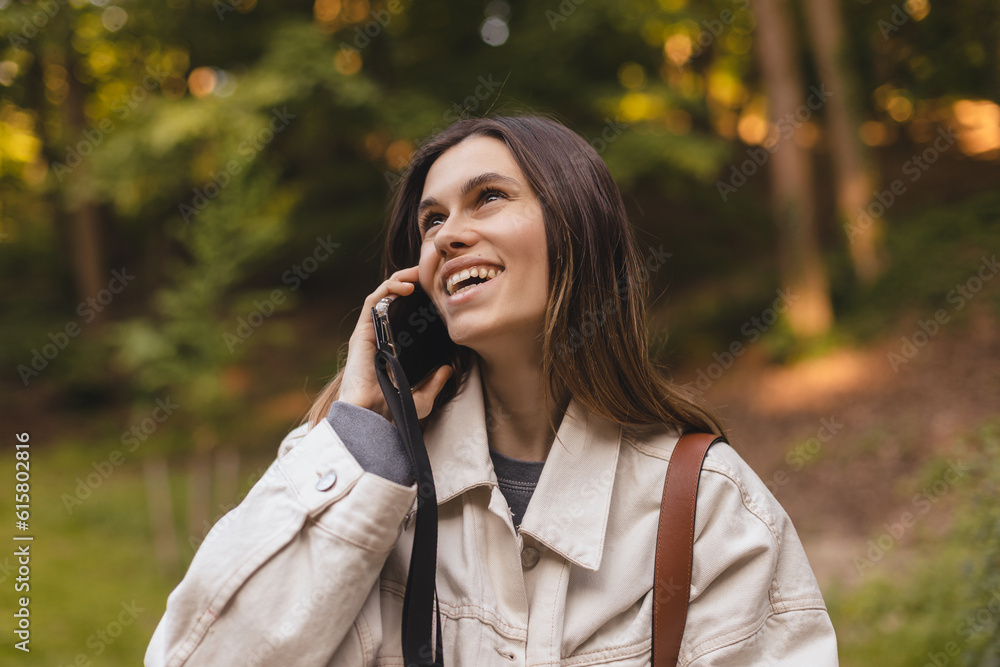 Happy brunette woman talking phone and look happy, smiling camera. Portrait of smiling female using mobile phone. Wow girl wear white jeans jacket and brown bag. Female walk on the street. Happy brunette woman talking phone and look happy, smiling camera. Portrait of smiling female using mobile phone. Wow girl wear white jeans jacket and brown bag. Female walk on the street.