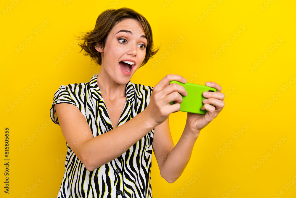 Portrait of impressed ecstatic woman wear zebra print blouse play amazing game app on smartphone isolated on yellow color background Portrait of impressed ecstatic woman wear zebra print blouse play amazing game app on smartphone isolated on yellow color background