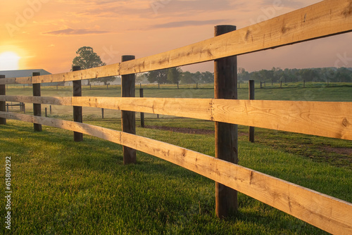 Sunrise lights an arching split rail fence on the farm