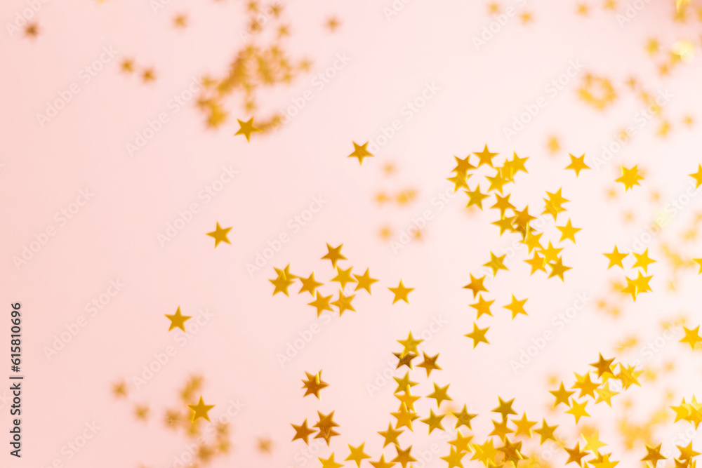 Pink background and gold confetti in the shape of stars. Beautiful holiday glitter