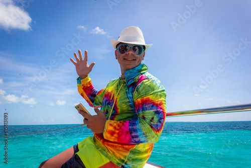 A caucasian man enjoying a summer sunny day on a boat at Isla Mujeres Cancun. Colorful clothing. happy young man smiling and waving.