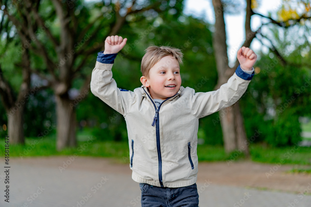 happy little caucasian boy triumphant with raised hands in park happy little caucasian boy triumphant with raised hands in park