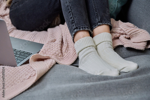 Close-up of legs in cozy woolen socks, laptop plaid sofa