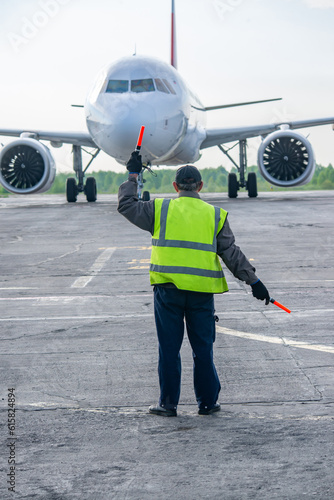 Ground Crew in the signal vest. Aviation Marshall Supervisor meets passenger airplane at the airport. Aircraft is taxiing to the parking place.