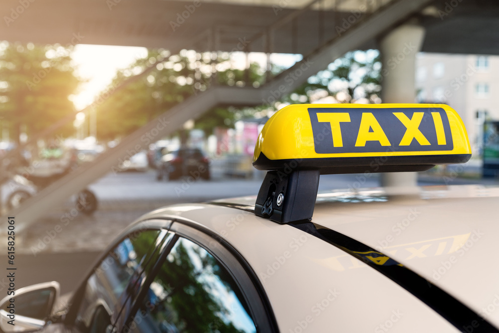 Close-up detail yellow taxi symbol on cars roof stand waiting at parking of airport terminal or railway station against park warm evening bokeh sunlight. Urban street transportation comfort service - obrazy, fototapety, plakaty 