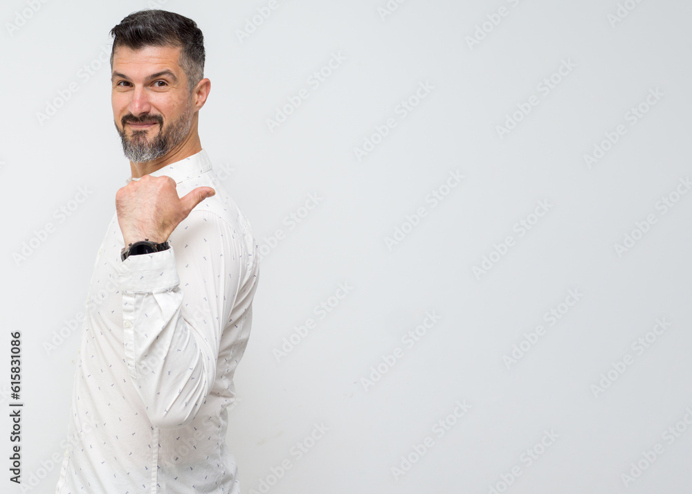 Happy adult smiling professional businessman wearing white shirt looking at camera pointing finger away at copy space showing aside presenting advertising offer standing isolated at gray. Happy adult smiling professional businessman wearing white shirt looking at camera pointing finger away at copy space showing aside presenting advertising offer standing isolated at gray.