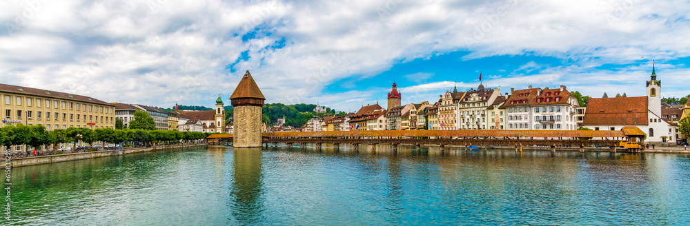 Full panoramic view of the famous diagonal covered timber footbridge Kapellbrücke (Chapel Bridge) with the Water Tower, spanning the river Reuss in Lucerne and the Old Town is in the background. 